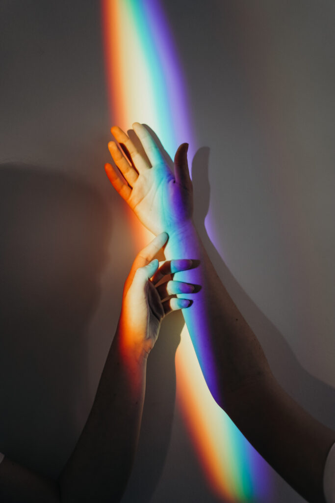 Two arms and hands mingle in a rainbow of light.